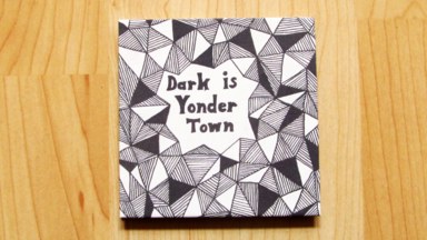 The front cover of the fold-out booklet. The words 'Dark is Yonder Town', surrounded by tesselated triangles.