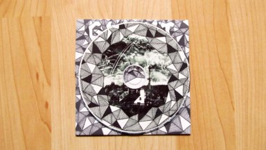 The CD itself, printed with a black and white collage framed by tesselated triangles.