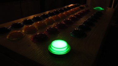 A shot of the controller in the dark, focused on the sole illuminated green arcade button.