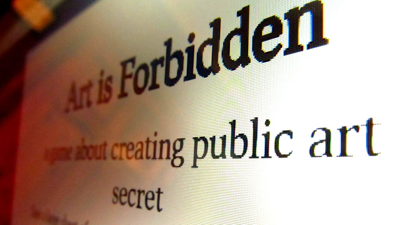 Close-up photograph of a computer screen with the Art is Forbidden pdf displayed. The words 'Art is Forbidden; a game about creating public art in secret' are visible.