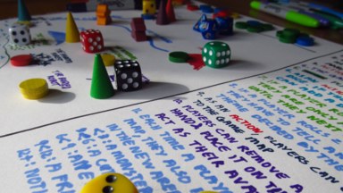 Close up of a game of making it up as we go along, with the rules in the foreground and the the player-created game board in the background